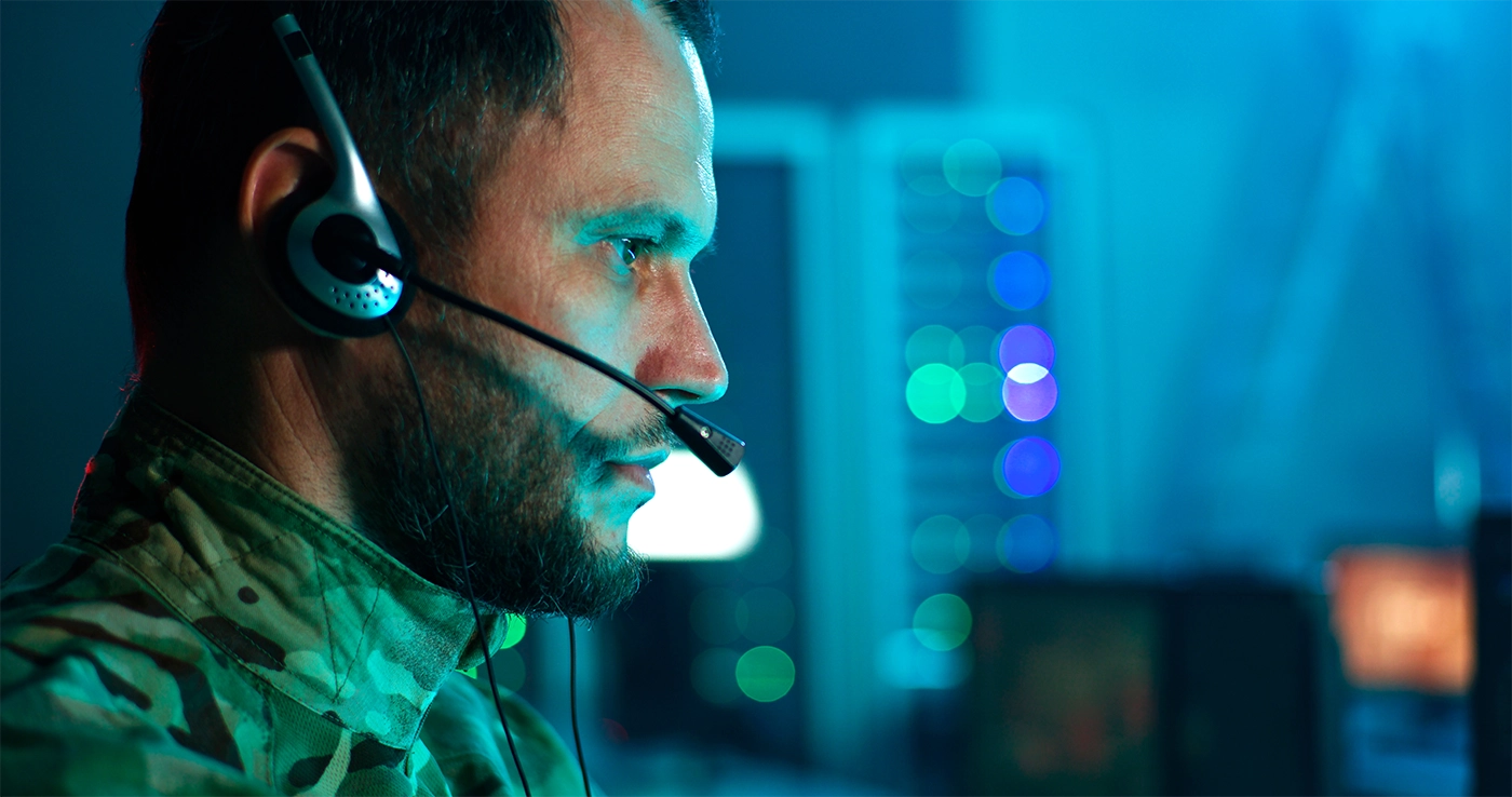 Military cyber security professional speaking on headset and using computer while working in network control center